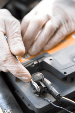 A gloved hand disconnecting an automotive battery wire from its terminal