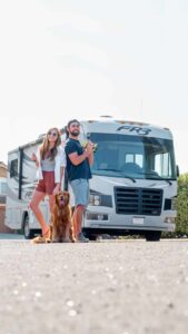 Young couple and their dog standing in front of a Class A motorhome