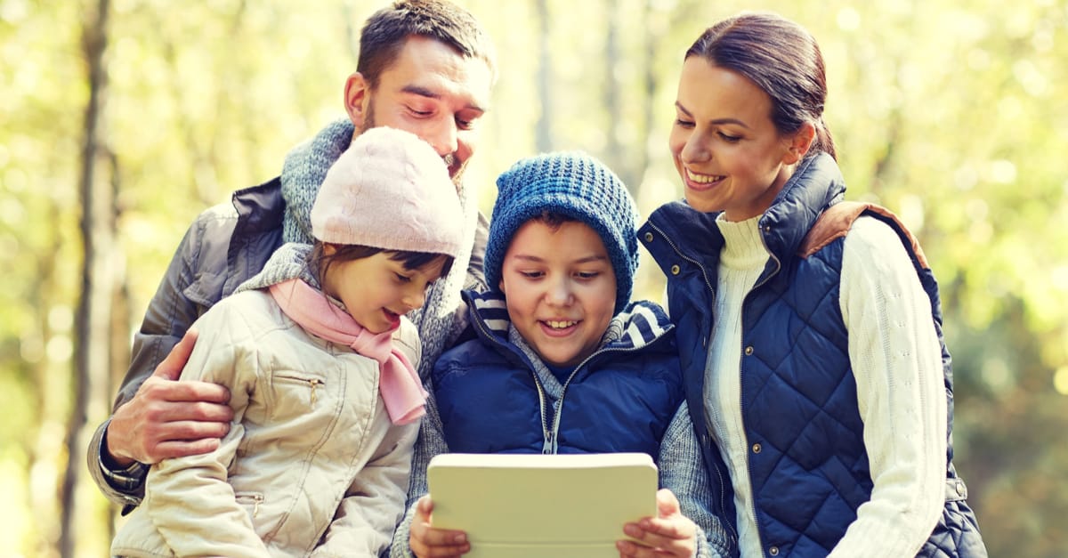 Family for 4 smiling and looking at a tablet