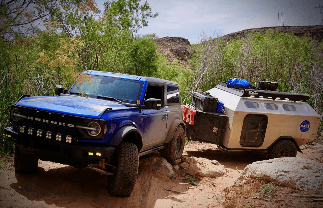 Bronco towing a small camping trailer.