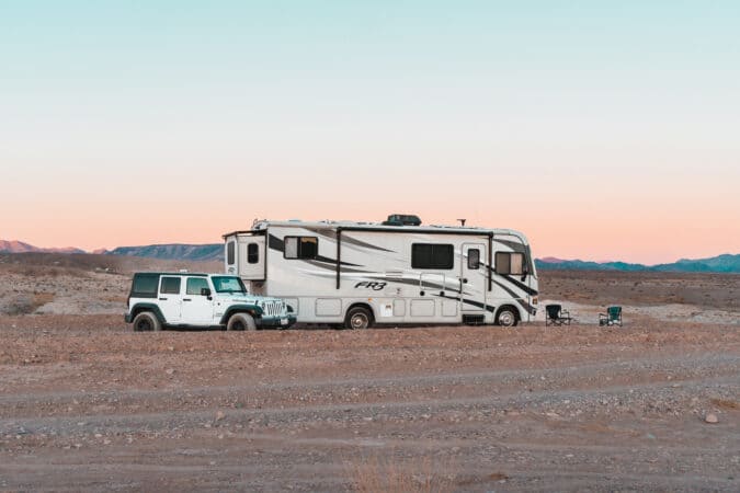 Motorhome and white Jeep parked in a desert with a cotton candy sky in the background.