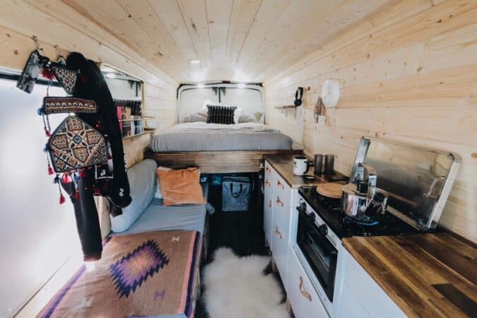 Inside of a camper van with a bed, bench, and counter with stove top