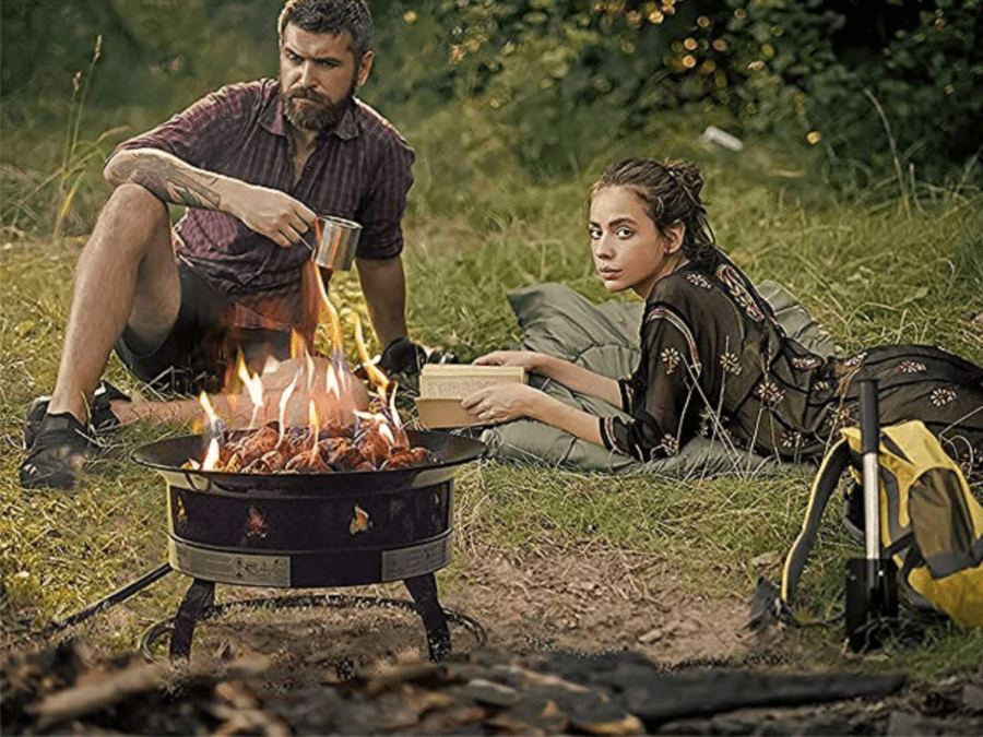 A couple enjoys their portable propane fire pit in the woods. 