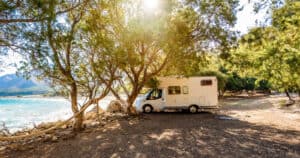 Motorhome RV parked on the beach under a tree facing the sea during summer camping
