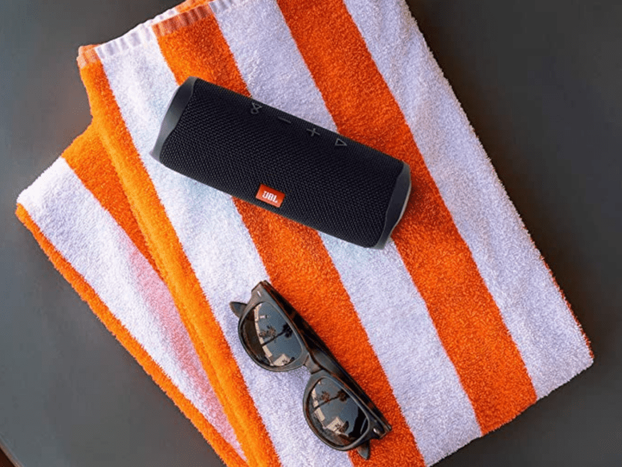 A JBL portable speaker and sunglasses on an orange and white beach towel.