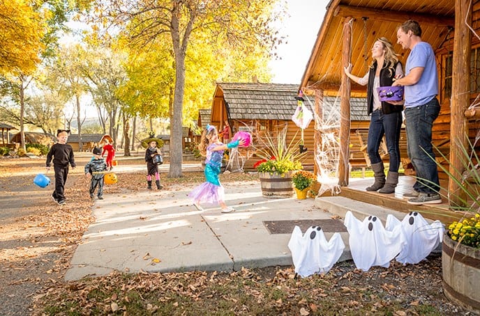 Couple handing out candy on porch of cabin with young children in Halloween costumes