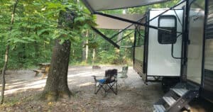 Travel Trailer set up in campsite in the woods with awnings and RV slide out extended.