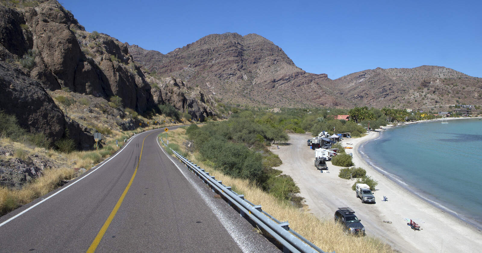 Winding narrow road with mountains in the background and vehicles and RVs camping in Baja California along the water