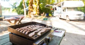 Camp kitchen set up with Bacon and sausage on a flat grill at an RV site