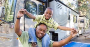 Father and son in front of RV. Son is sitting on father's shoulders. RV living with kids can be a fun and memorable experience.