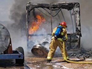 RV metal frame burning with firefighter fighting the flames in the forefront