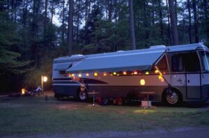 Motorhome with the awning out and decorative lanterns strung around it. parked in a wooded RV site.