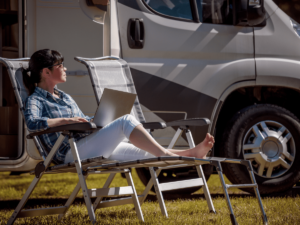 A woman soaks up the sun and works on her laptop outside of her RV.