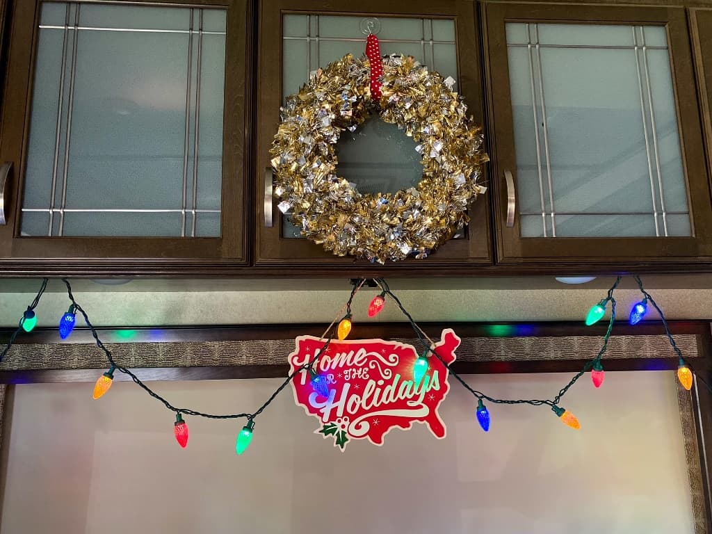 A Christmas wreath, holiday lights and holiday sign hanging from RV cabinet