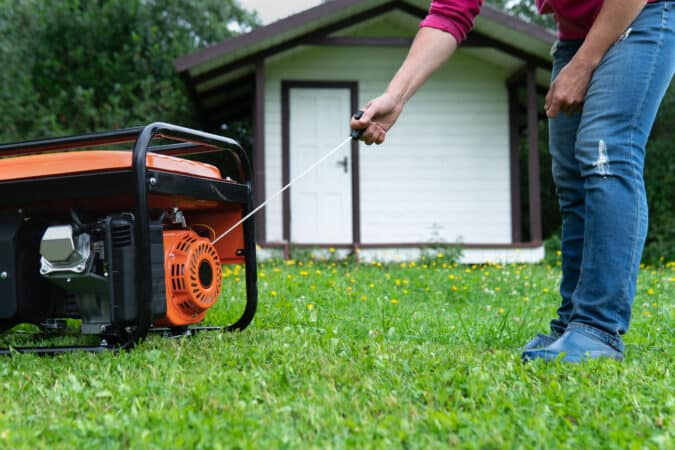Woman pulling the start cord on a generator in the grass