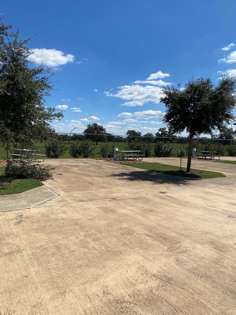 Empty RV site with a concrete pad, picnic table, and surrounding greenery under a clear blue sky at Brazoria Lakes RV Resort.