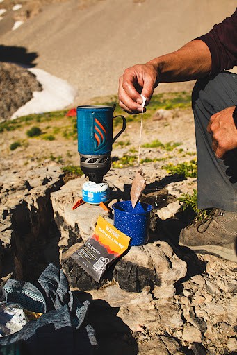 Camper steeps Wildland Coffee bag in cup over campfire.