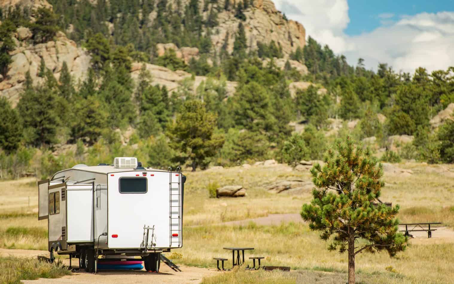 A fifth wheel RV parked in a field with a mountain in the background