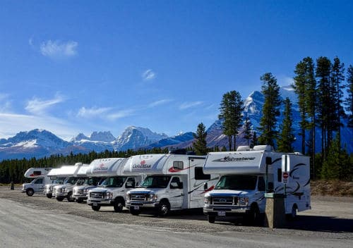 row of Class C motorhomes for sale in a parking lot surrounded by mountains