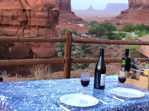 A camp kitchen tablecloth on an outdoor table with wine and dishes.