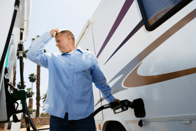 A man filling up his RV at the gas pump and scratching his head