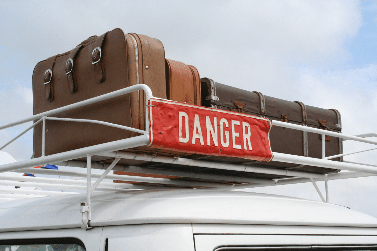 Various pieces of luggage on the roof rack of a camper, along with a sign reading “danger”