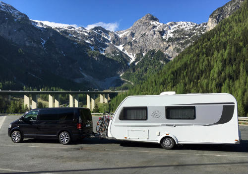 van towing a travel trailer parked in a parking lot surrounded by mountains