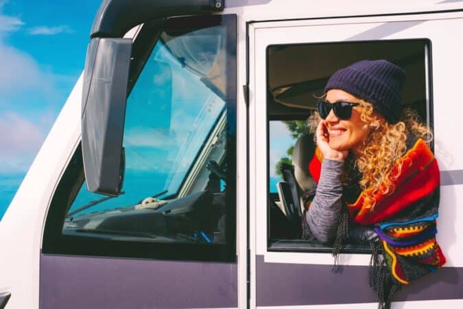 Cheerful and happy adult pretty woman outside the window of her camper van motorhome enjoy alternative travel and free nomadic lifestyle.