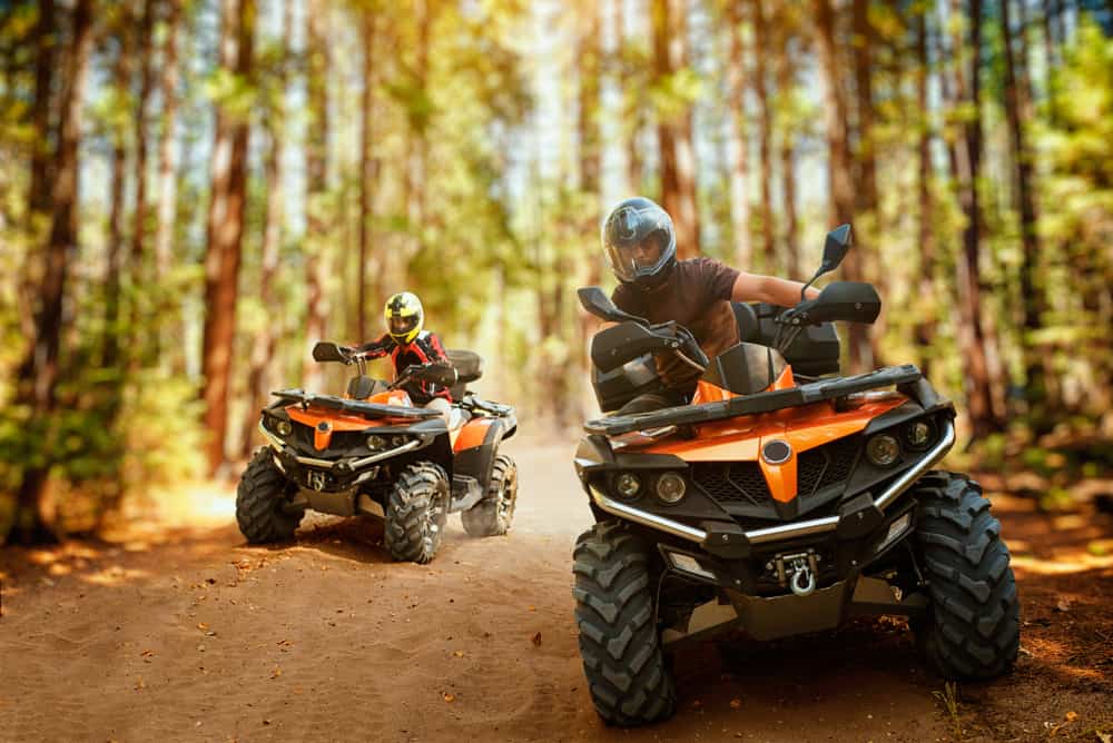 Two ATVs ride in a forest trail as part of the RV community