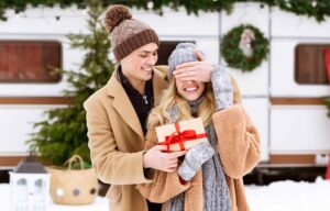 Young couple exchanging holiday gifts in front of RV