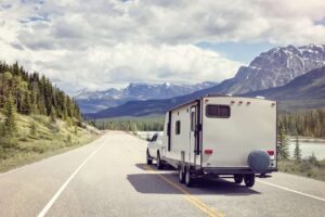 A truck and RV travel down a scenic highway with stream and mountian