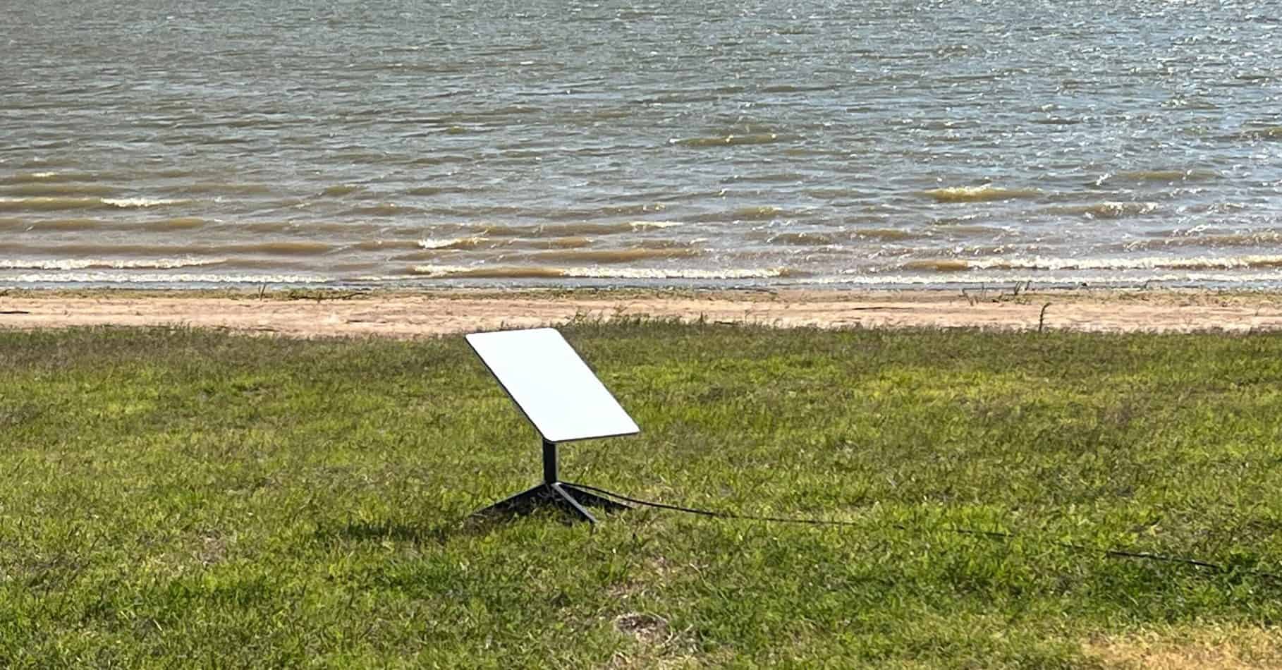 A Starlink Antenna sits near the shore at a remote campground.