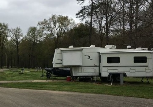 White fifth wheel is parked in a campground