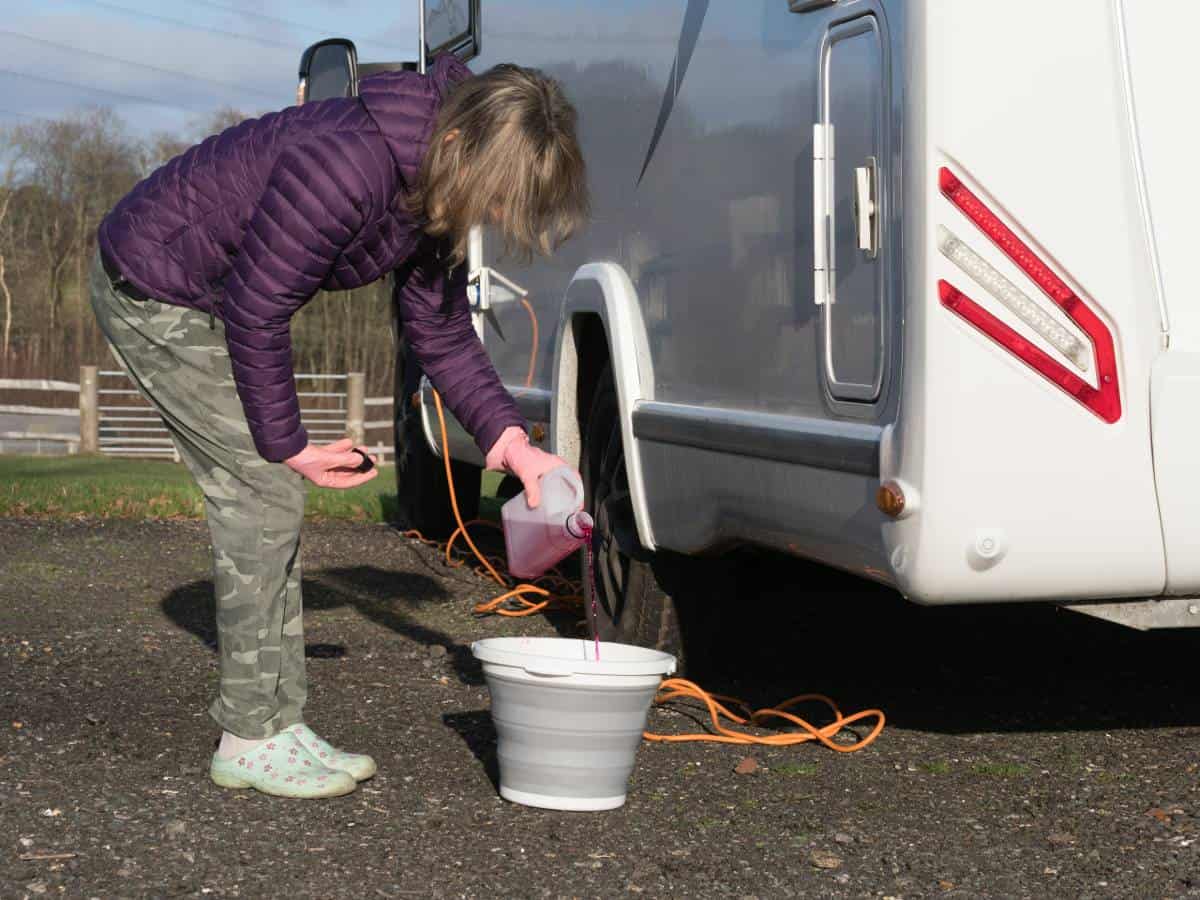 Woman pouring liquid in bucket next to motorhome